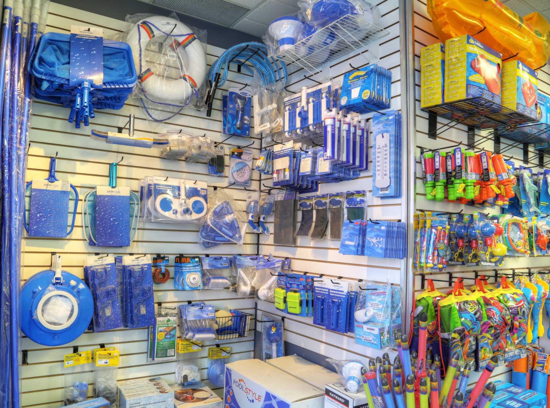 A store display featuring various pool accessories: nets, floats, and water toys, showcasing a vibrant assortment of blue and colorful items.