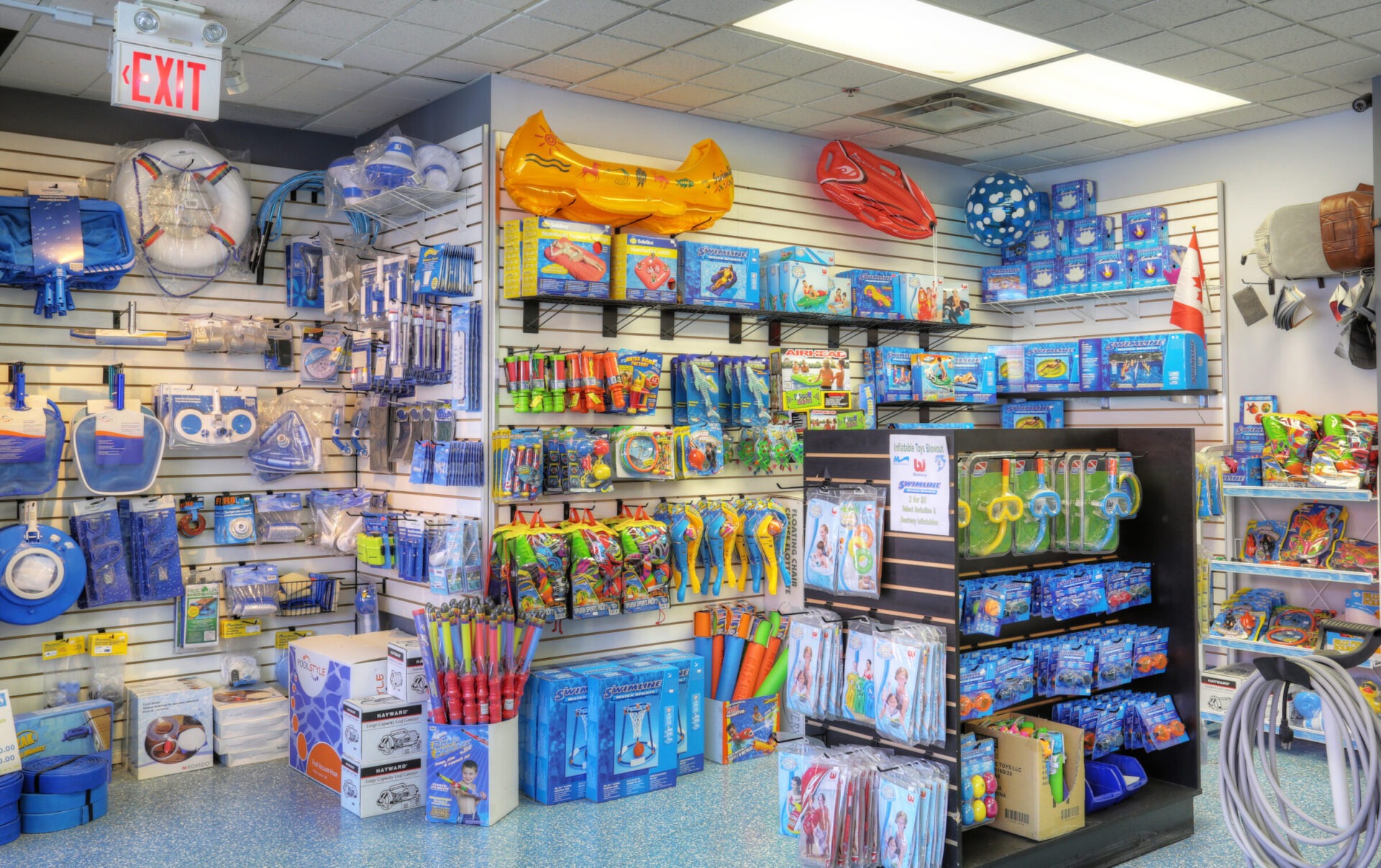 A store interior featuring colorful pool supplies, toys, and inflatables on display. Shelves are neatly arranged with various swimming and diving accessories.