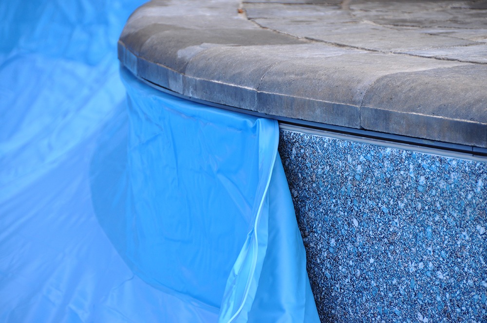 Close-up of a pool with a blue tarp partially covering the stone edge. No people or recognizable landmarks are visible.