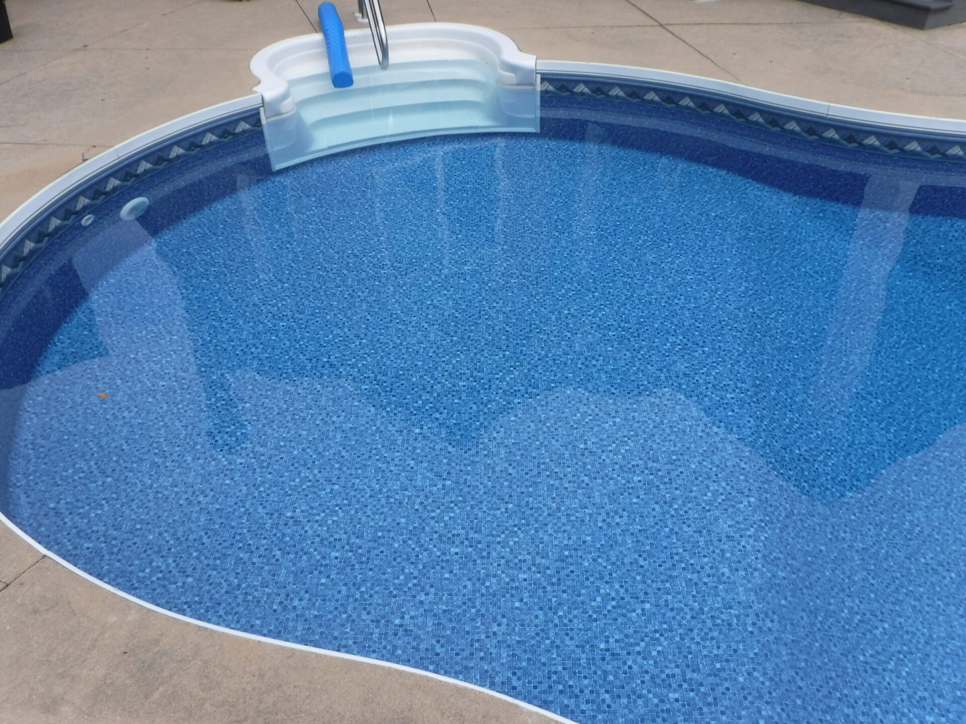 A clear, oval-shaped swimming pool with blue water, steps at one end, and a concrete patio surrounding it. No people are present.